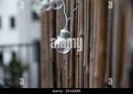 LED mint color light bulbs with wires hanging on a bamboo screen wall outside on a deck Stock Photo
