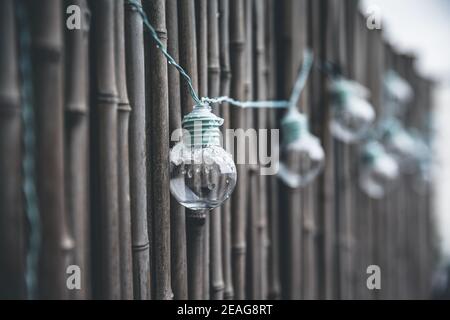 LED mint color light bulbs with wires hanging on a bamboo screen wall outside on a deck Stock Photo