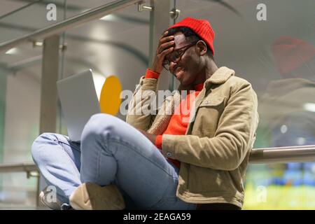 Black man sitting on the floor talking in video chat on laptop chatting in social networks, smiling Stock Photo