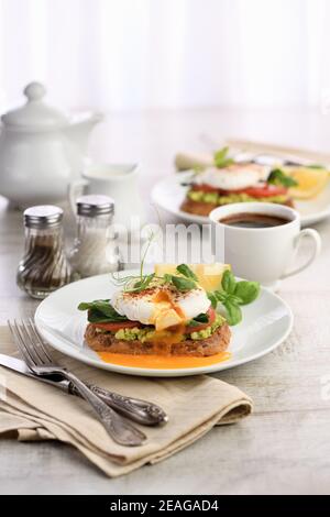 Breakfast. Best Eggs Benedict on a slice of toasted cereal bread with guacamole and spinach Stock Photo