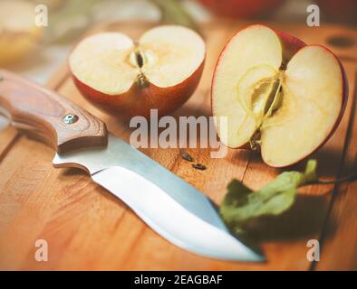 A red ripe delicious juicy apple was cut with a sharp knife and its halves lie on a wooden kitchen board, illuminated in sunlight on a summer day. Har Stock Photo