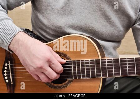 Man playing on acoustic guitar. Close up view of guitarist hands and guitar body while practicing and training on the instrument. Stock Photo