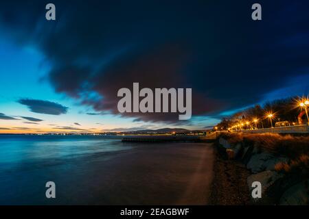 Evening on sea resort after sunset, colorful cloudy sky above sea waves and coastline in twilight. Stock Photo