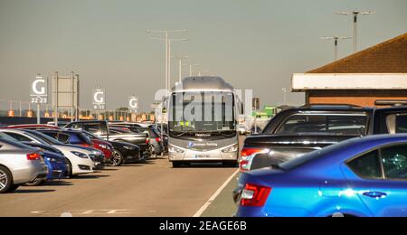 London, England - August 2018: Shuttle bus driving between rows of parked cars in an airport business car park. Stock Photo