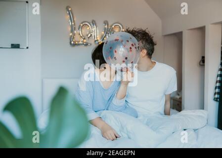 Couple kissing behind a red heart balloons with Sunlight Stock Photo