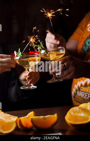 Celebrating new year eve 2022 with sparklers fireworks and drinking cocktails. Mint with orange slice in a cocktail glass filled with alcohol cocktail Stock Photo