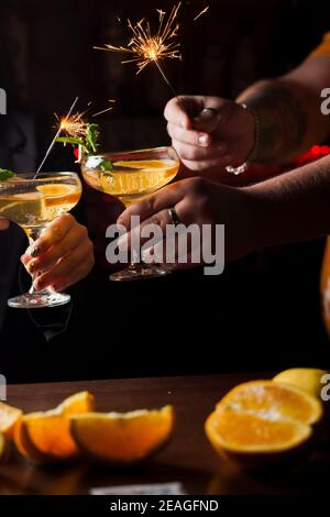 Celebrating new year eve 2022 with sparklers fireworks and drinking cocktails. Mint with orange slice in a cocktail glass filled with alcohol cocktail Stock Photo