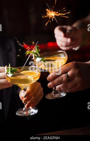 Celebrating new year eve 2022 with sparklers fireworks and drinking cocktails. Mint with orange slice in a cocktail glass filled with alcohol cocktail Stock Photo