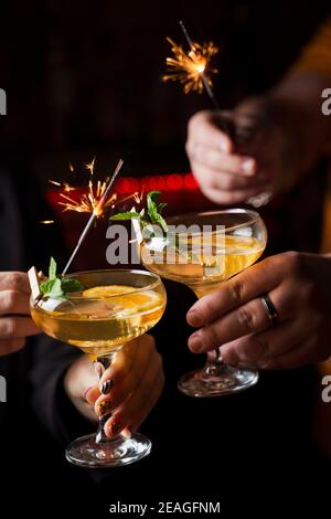 Celebrating new year eve 2022 with sparklers fireworks and drinking cocktails. Mint with orange slice in a cocktail glass filled with alcohol cocktail Stock Photo