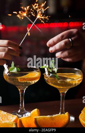 Celebrating new year eve 2022 with sparklers fireworks and drinking cocktails. Mint with orange slice in a cocktail glass filled with alcohol cocktail Stock Photo