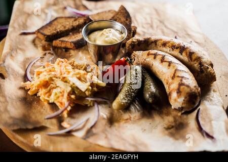 Grilled sausages with beer and vegetables with pickled cucumber, cabbage salad sauce and bread on parchment, top view. Stock Photo