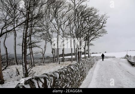 Man walking along a snow covered road at Longstone Edge in the Peak District Stock Photo