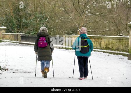 Two women Nordic walking in the snow using trekking poles. They are enjoying daily exercise hiking on Hampstead Heath as a socially distanced walk. UK Stock Photo