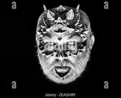 Demon head on black background. Alien or reptilian makeup. Monster with sharp thorns and warts on face. Man with dragon skin and grey beard. Horror Stock Photo