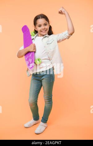 I can ride it. Kid girl happy holds penny board. Girl happy face carries penny board yellow background. Child learned ride penny board. Kid likes plastic skateboard shows power gesture. Girls power. Stock Photo