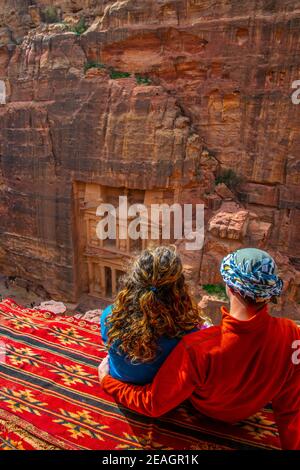 Young couple sitting at a viewpoint on Al Khazneh tomb also called Treasury at Petra, Jordan Stock Photo
