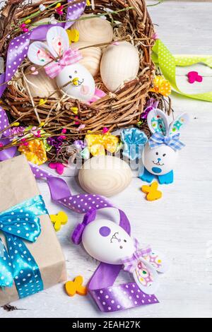 Handmade traditional Easter symbols concept. Cute rabbits from eggs in basket, wicker wreath with flowers, festive decor. White wooden background, clo Stock Photo