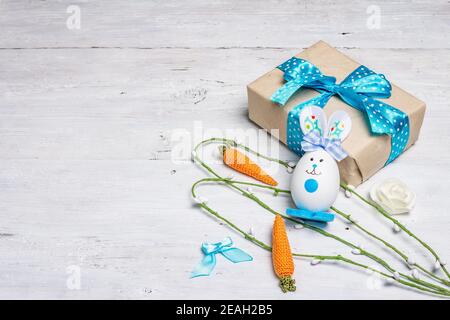 Handmade traditional Easter symbols concept. Cute rabbit from the egg, gift box, festive decor in blue tones. White wooden background, copy space Stock Photo