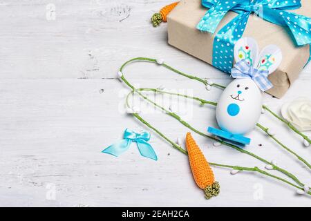 Handmade traditional Easter symbols concept. Cute rabbit from the egg, gift box, festive decor in blue tones. White wooden background, top view Stock Photo