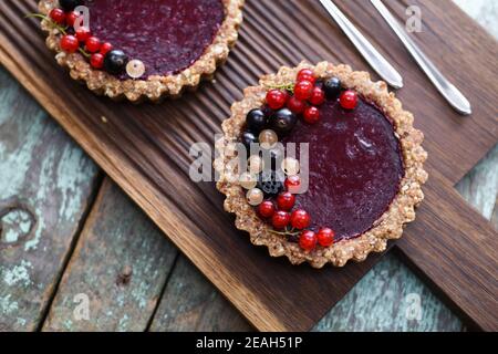 Small vegan tarts made of nuts and berry jam decorated with black, red and white currants on oak cutting board copyspace above view Stock Photo