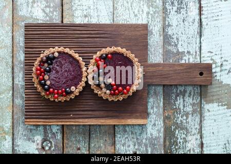 Small vegan tarts made of nuts and berry jam decorated with black, red and white currants on oak cutting board copyspace Stock Photo