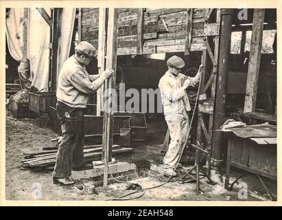 FRAUREUTH, EAST GERMANY - MAY 21, 1965: The retro photo shows building site in Communist bloc. Two bricklayers measures with water level. Former East Stock Photo