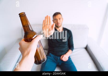 No alcohol. Young man refuses to drink beer, making stop gesture to bottle of beer Stock Photo