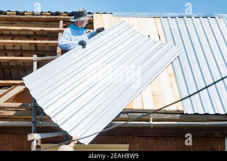 two people, carpenters, builders, lay a galvanized sheet of iron on the roof of the house Stock Photo
