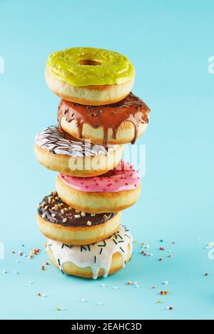Multicolored donuts with icing and sprinkling stacked in a stack on a blue background. Stock Photo