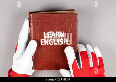 Learn English concept. Leather work gloves in hand and a textbook on a gray background. Stock Photo