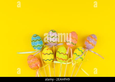 Multicolored Easter eggs on sticks on yellow background. Festive Easter holiday greeting card with copy space. Stock Photo