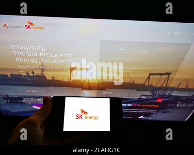 Person holding smartphone with business logo of South Korean oil company SK Energy on screen in front of website. Focus on phone display. Stock Photo