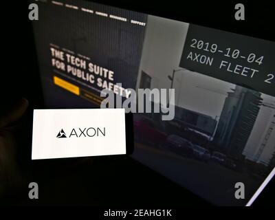 Person holding smartphone with logo of American weapon manufacturer Axon Enterprise Inc. on screen in front of website. Focus on phone display. Stock Photo