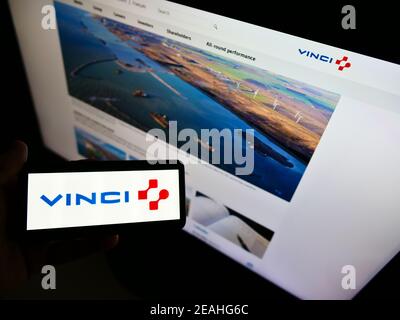 Person holding smartphone with logo of French concessions and construction company Vinci S.A. on screen in front of website. Focus on phone display. Stock Photo