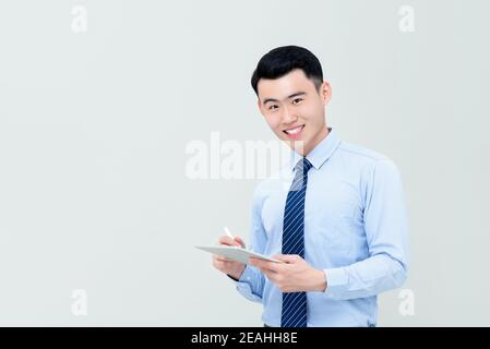 Young smiling Asian businessman using digital tablet with stylus pen isolated on gray background Stock Photo