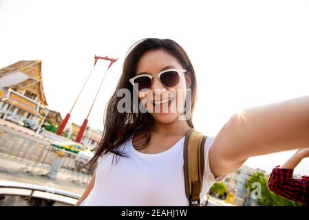 Asian tourist woman taking selfie while traveling in Bangkok Thailand with Giant Swing and Buddhist temple in background Stock Photo