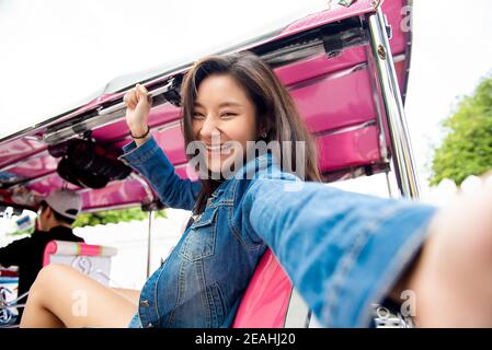 Pretty Asian tourist woman taking selfie on local Tuk Tuk taxi while solo traveling in Bangkok city Thailand Stock Photo