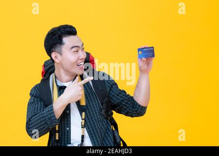Happy Asian tourist backpacker smiling and pointing to credit card isolated on yellow backround Stock Photo