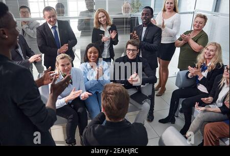 Office employees sit on chairs clap hands greeting presenter or speaker at group meeting close up. Stock Photo
