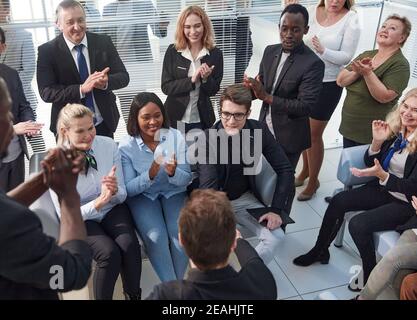 Office employees sit on chairs clap hands greeting presenter or speaker at group meeting close up. Stock Photo