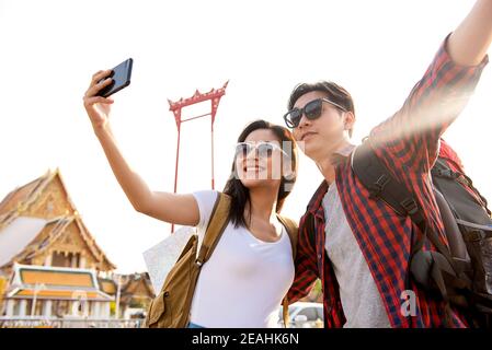 Asian couple tourists taking selfie while traveling in Bangkok Thailand with Giant Swing and Buddhist temple in background Stock Photo