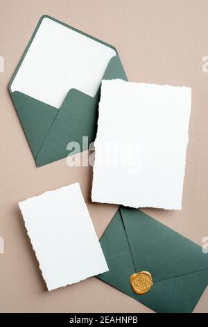 Elegant wedding invitation cards mockups and green envelopes on brown background. Flat lay, top view, copy space. Stock Photo