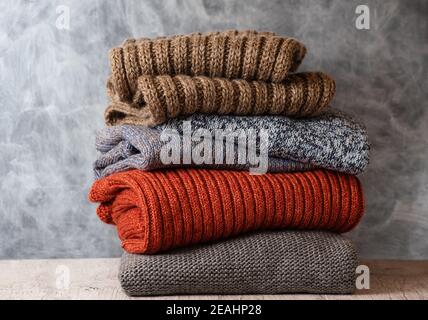 Pile of folded knitted warm women sweaters and scarves on gray background. Soft comfortable cozy knitwear. Copy space Stock Photo