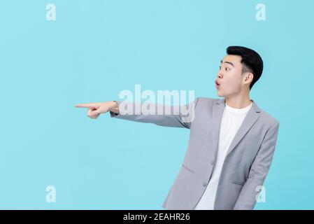 Young handsome Asian businessman in smart casual clothes looking surprised and amazed pointing hand to copy space isolated on light blue background Stock Photo