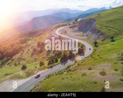 Red car driving on winding road through snowy forest, sunlight aerial ...