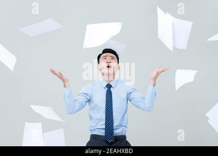 Busy Asian business man overwhelmed by too much work and surrounded by flying paper Stock Photo