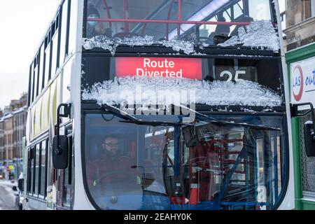 Edinburgh, Scotland, UK. 10 Feb 2021. Big freeze continues in the UK with heavy overnight and morning snow bringing traffic to a standstill on many roads in the city centre. Pic; Lothian bus covered in snow slowly makes way up Leith Walk with diversions in place because of snow . Iain Masterton/Alamy Live news
