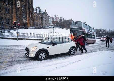 Edinburgh, Scotland, UK. 10 Feb 2021. Big freeze continues in the UK with heavy overnight and morning snow bringing traffic to a standstill on many roads in the city centre. Pic; People push car up The Mound to clear path for bus.  Iain Masterton/Alamy Live news Stock Photo