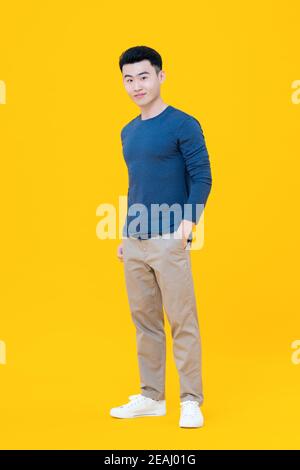 Young cute Asian man standing with hand in pocket gesture isolated on yellow background Stock Photo