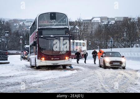Edinburgh, Scotland, UK. 10 Feb 2021. Big freeze continues in the UK with heavy overnight and morning snow bringing traffic to a standstill on many roads in the city centre. Pic; People push car up The Mound to clear path for bus.  Iain Masterton/Alamy Live news Stock Photo